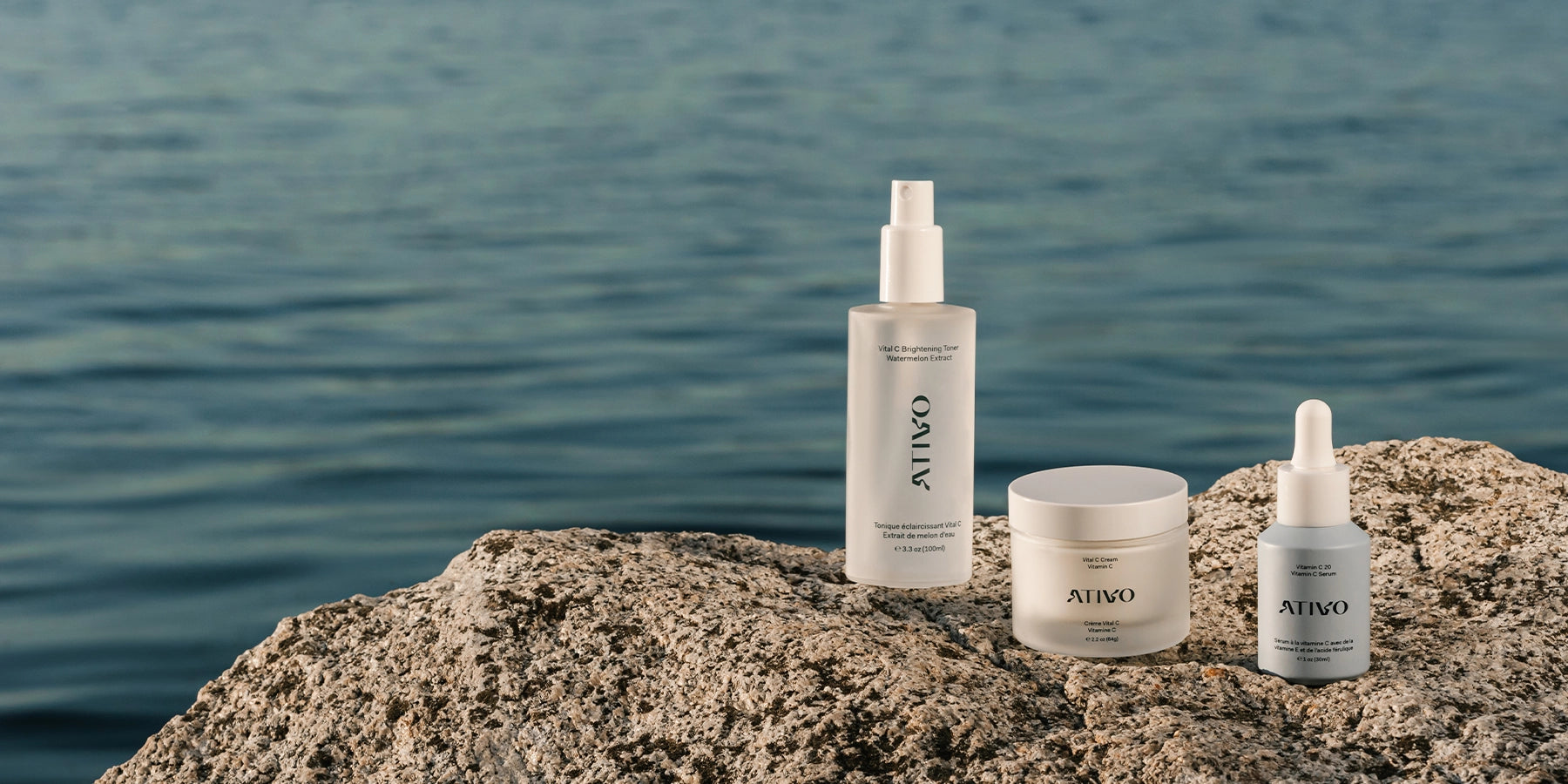 Three skincare items sitting on a rock with the ocean in the background. 