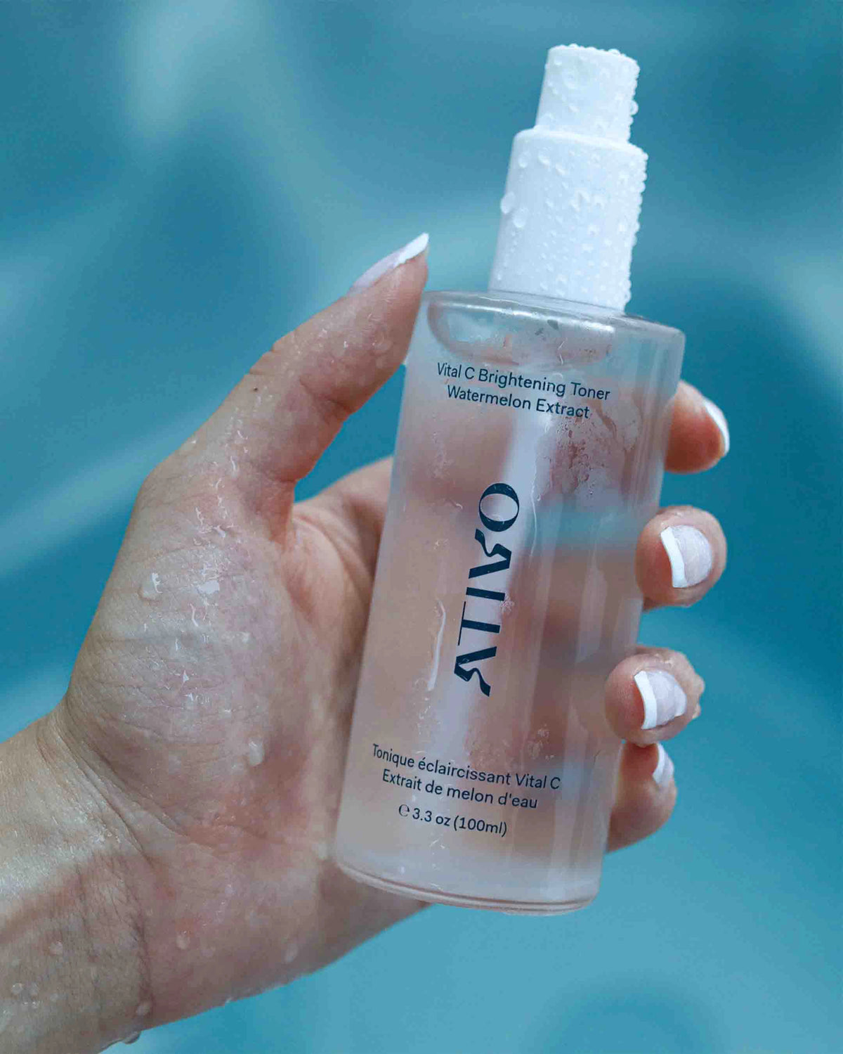 Vital C brightening toner in a clear, frosted bottle in a woman&#39;s hand with water, droplets all over